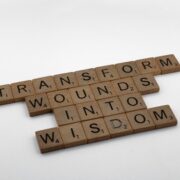 Scrabble tiles spelling 'Transform wounds into wisdom,' representing the science behind coaching and personal transformation.