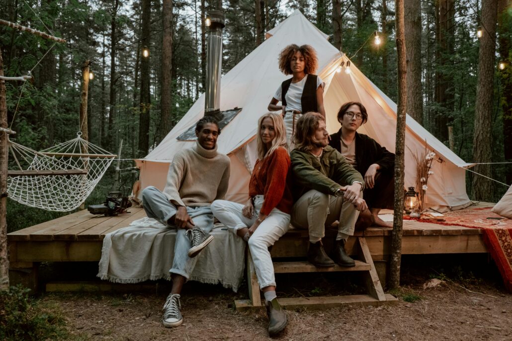 A diverse group of young adults sitting together in front of a glamping tent in the forest, symbolizing connection, reflection, and community at a life coaching retreat.