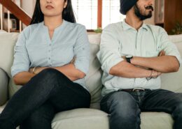 Couple sitting on a couch with arms crossed, showing tension during a difficult conversation, illustrating conflict resolution coaching.