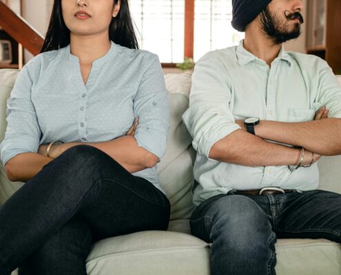 Couple sitting on a couch with arms crossed, showing tension during a difficult conversation, illustrating conflict resolution coaching.