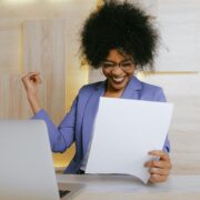 Smiling woman sitting in front of a laptop, celebrating a breakthrough moment, symbolizing the success of using powerful coaching tools in a session.