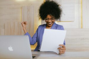 Smiling woman sitting in front of a laptop, celebrating a breakthrough moment, symbolizing the success of using powerful coaching tools in a session.