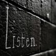 Word 'Listen' written on a dark brick wall, symbolizing the power of active listening in coaching to build trust and transformation.